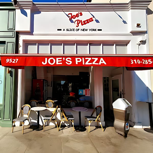 The exterior of Joe's Pizza, a New York-style pizzeria, with outdoor seating under a red awning.