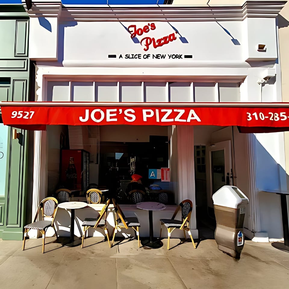 The exterior of Joe's Pizza, a New York-style pizzeria, with outdoor seating under a red awning.