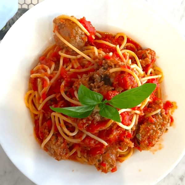 Spaghetti with meatballs and tomato sauce, garnished with fresh basil, served in a white bowl.