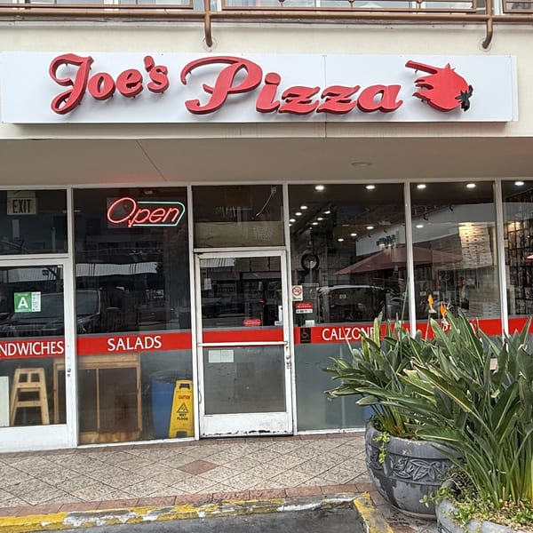 Joe's Pizza storefront with a red neon 'Open' sign, glass doors, and potted plants outside.