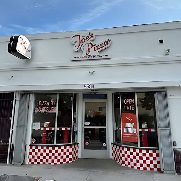 The exterior of Joe's Pizza, a white building with red and white checkered trim, under a blue sky.