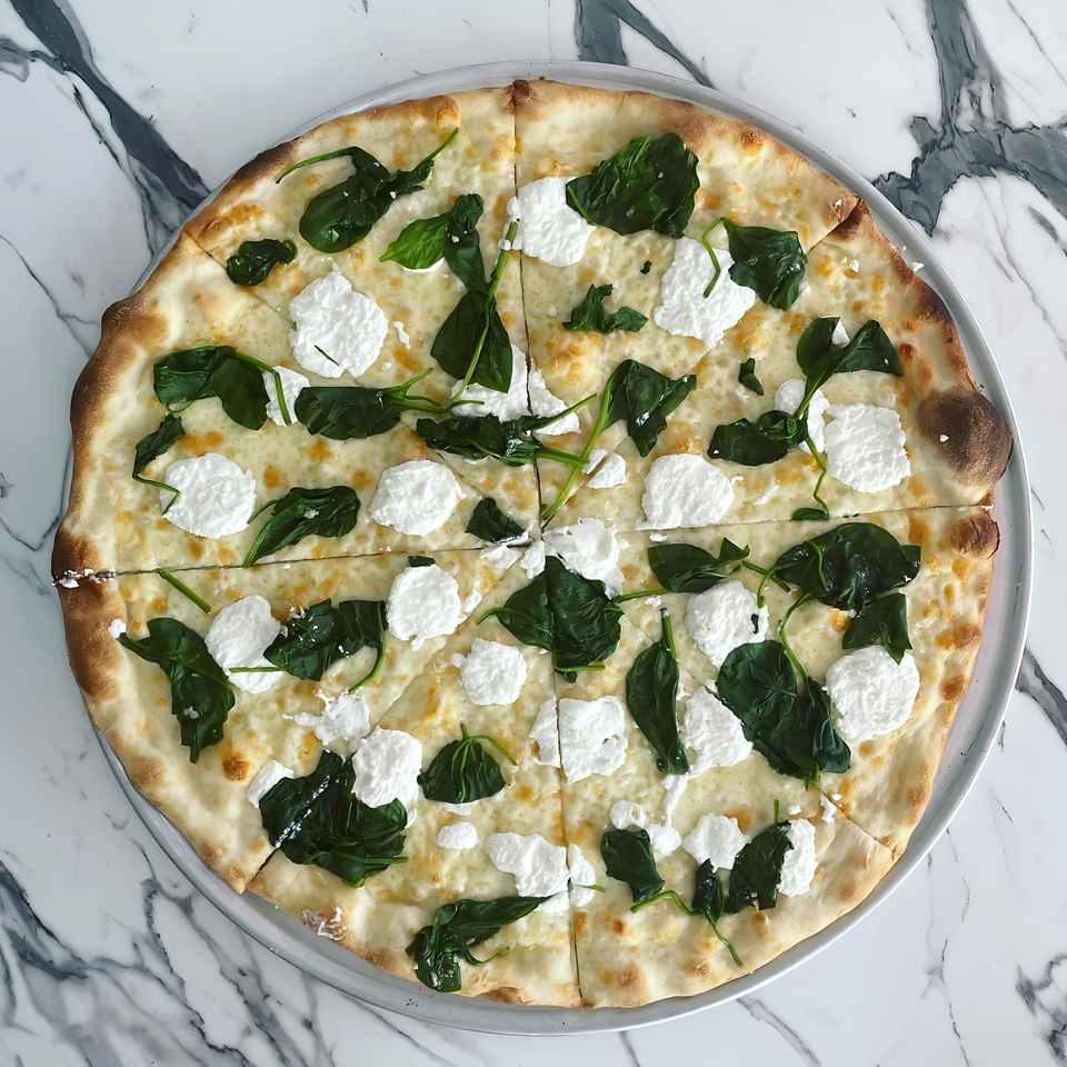 A white pizza from Joe's Pizza with spinach and dollops of ricotta cheese on a marble surface.