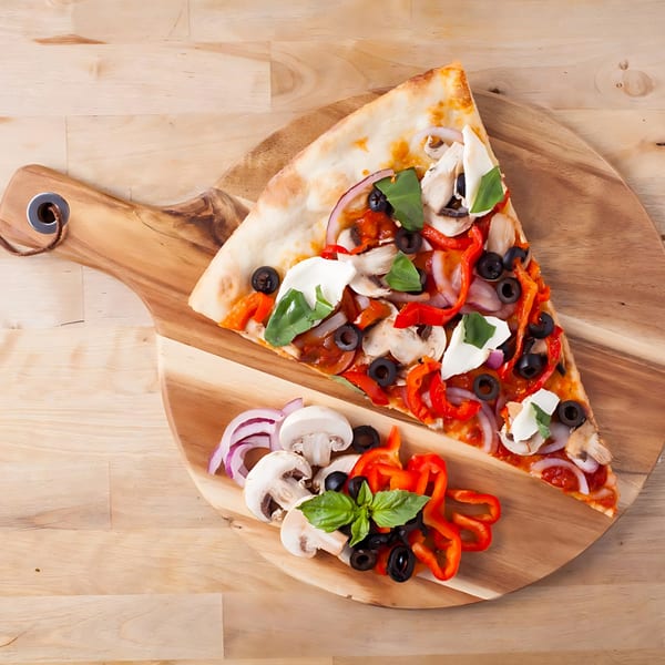 A slice of Joe's pizza with mushrooms, olives, red peppers, onions, and basil on a wooden board.