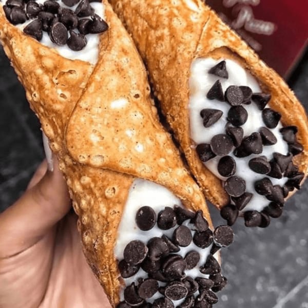 Two Joe's Pizza cannolis filled with white cream and topped with chocolate chips.