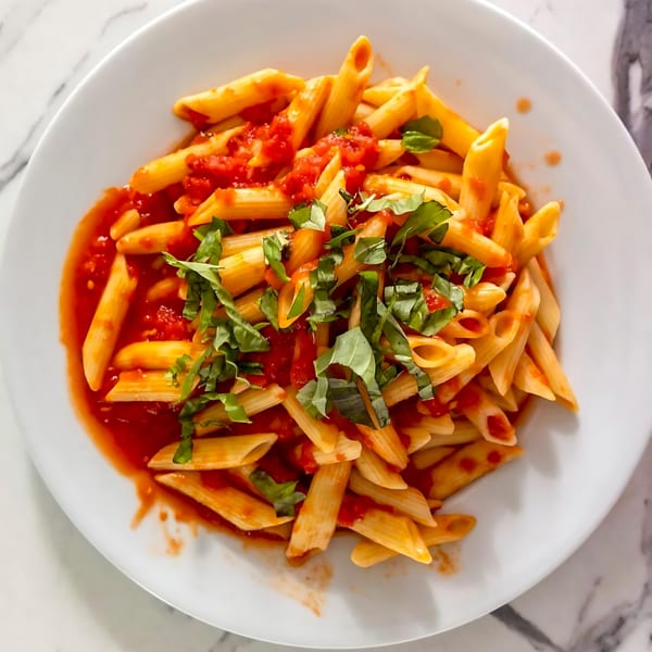 Penne pasta with red tomato sauce and fresh basil on a white plate.