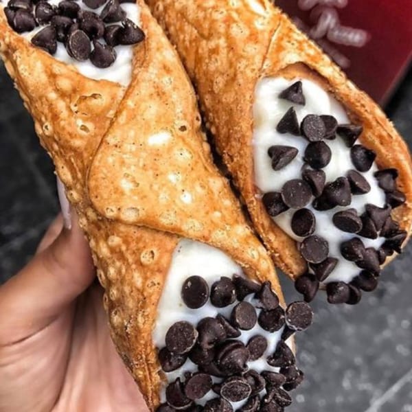 Two Joe's Pizza cannolis filled with white cream and topped with chocolate chips.