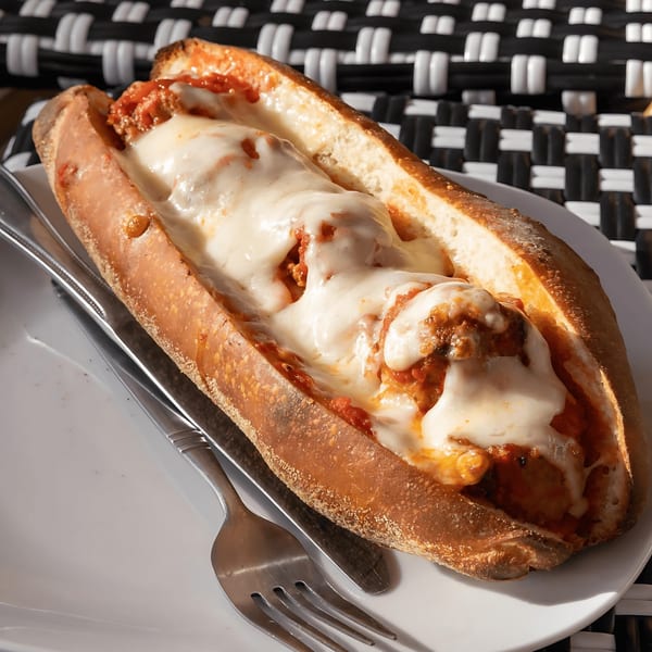 A Joe's Pizza meatball sub with melted cheese and marinara sauce on a white plate.