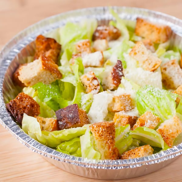 Joe's Pizza Caesar salad in a foil container, with crisp lettuce, croutons, and grated cheese.