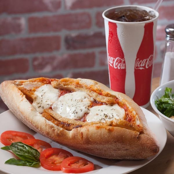 Joe's pizza chicken parmesan hero with melted mozzarella, a Coca-Cola, and a side salad.