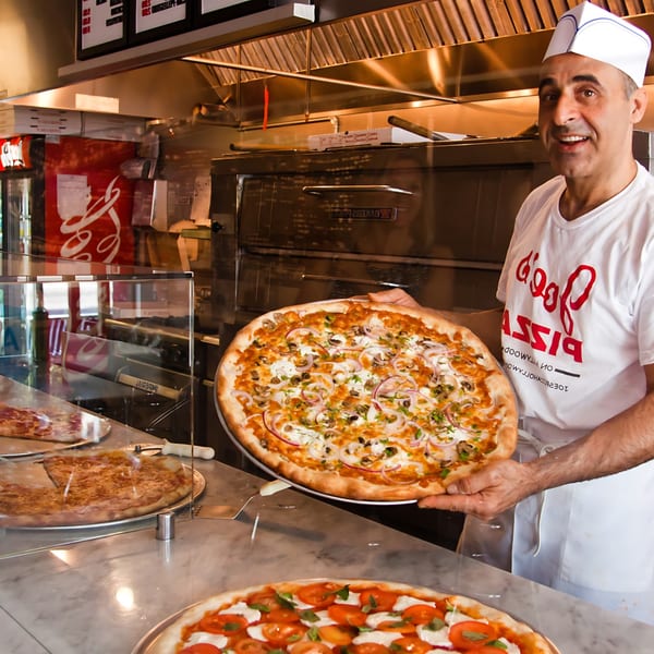 Joe's Pizza chef in a white hat and shirt holding a fresh mushroom and onion pizza.