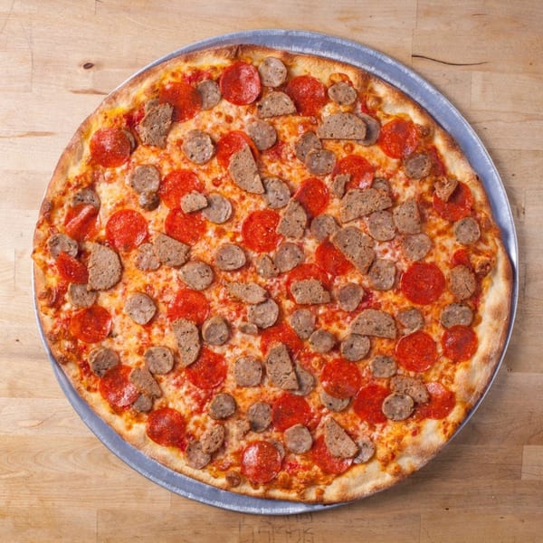 Joe's pizza with pepperoni and sausage toppings on a metal pan, on a wooden surface.