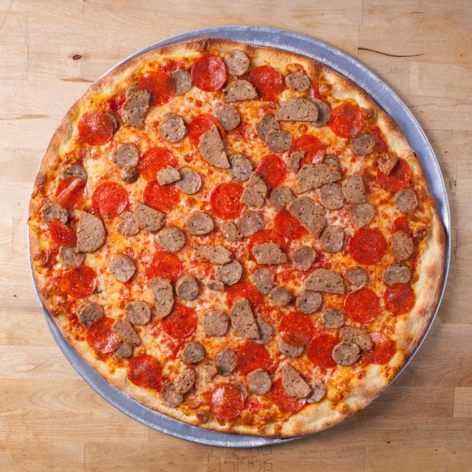 Joe's pizza with pepperoni and sausage toppings on a metal pan, on a wooden surface.