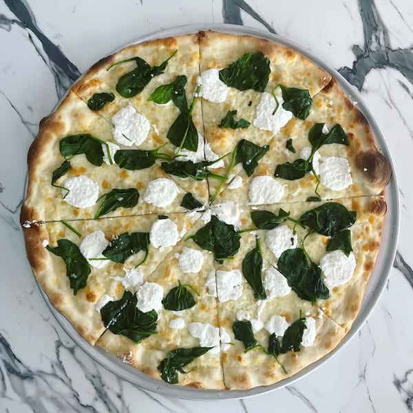 Joe's pizza with white sauce, mozzarella, ricotta, and fresh spinach on a marble surface.