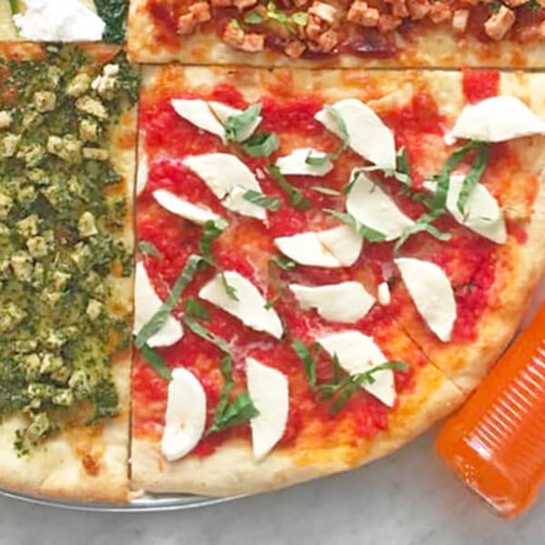 Close-up of Joe's Pizza with various slices, including Margherita and pesto, and a hot sauce bottle.