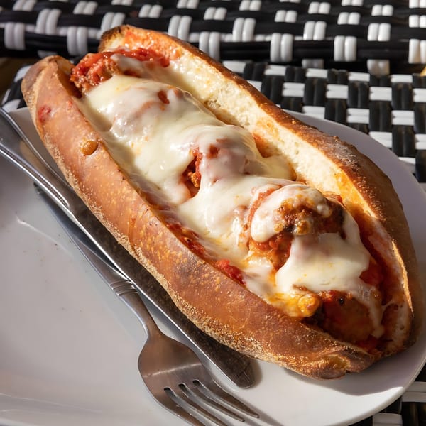 Joe's Pizza meatball sub with melted mozzarella cheese and marinara sauce on a white plate.