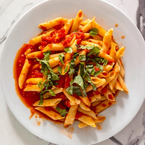 Penne pasta with red tomato sauce and fresh basil on a white plate.
